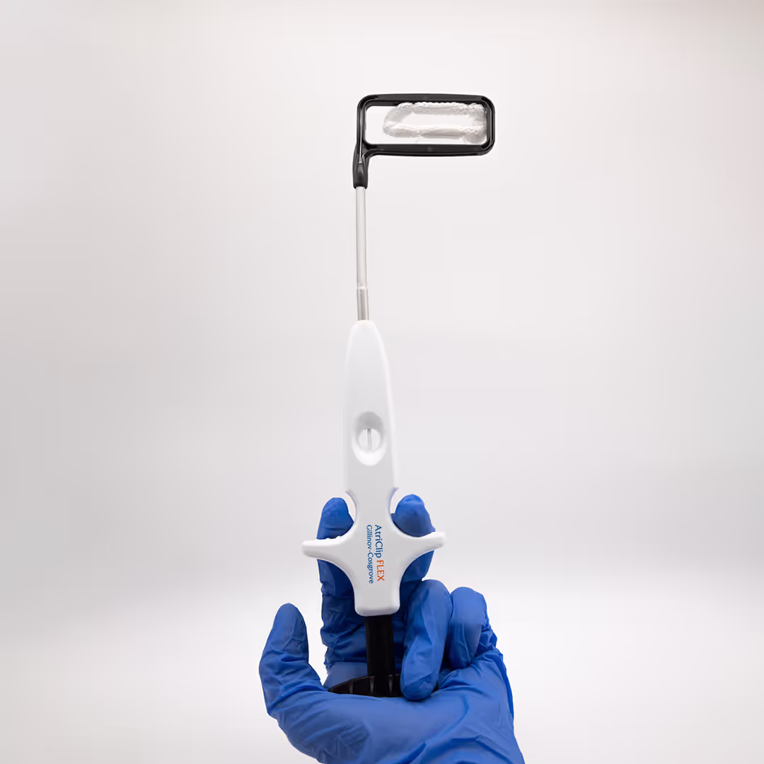 Dispositivo de oclusão da auriculeta atrial esquerda AtriClip Flex sendo segurado por uma mão com luva cirúrgica, mostrando seu cabo, haste e o clipe na ponta.