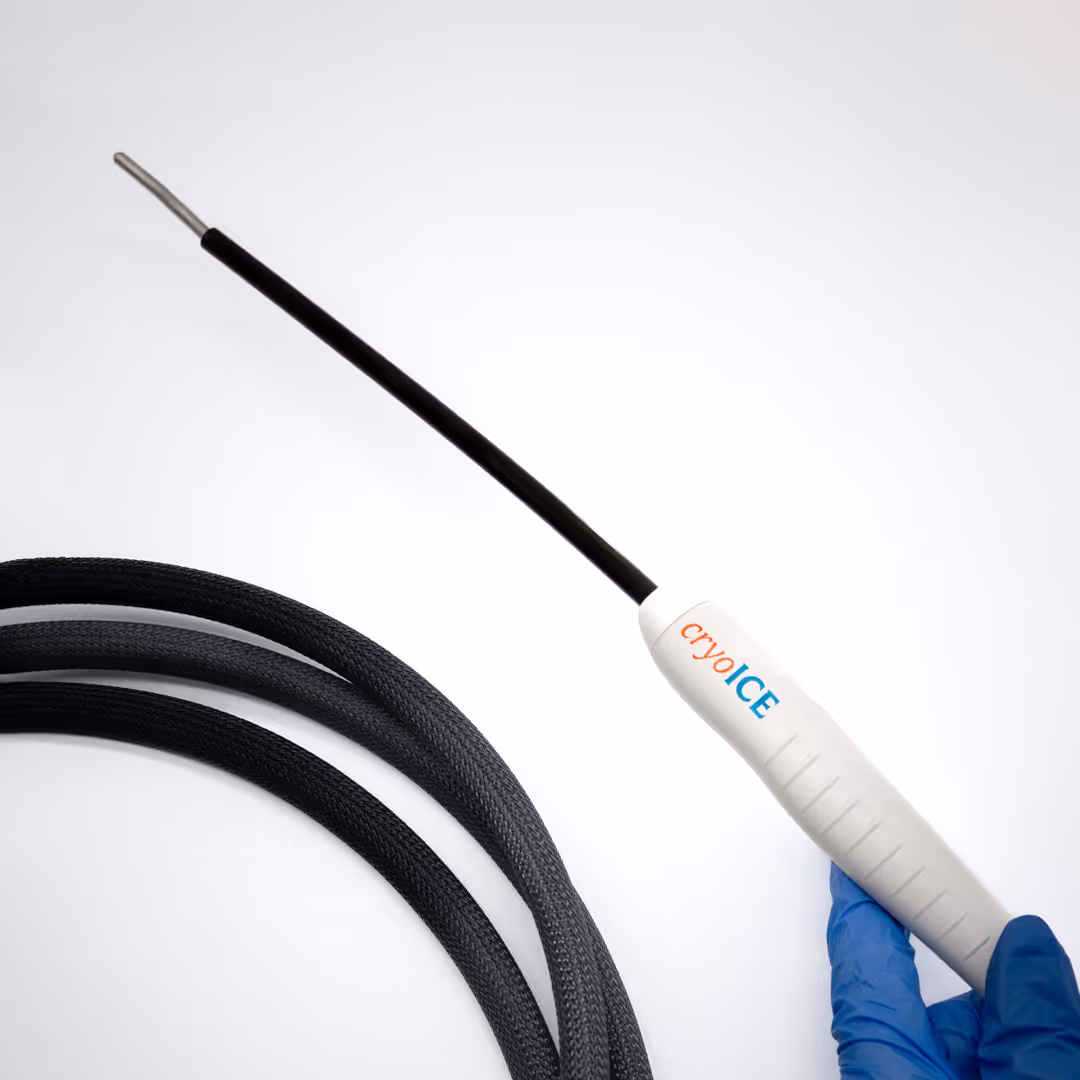 Mão com luva cirúrgica azul segurando a sonda de crioablação CryoICE, com sua haste preta e ponta metálica em destaque sobre um fundo branco.