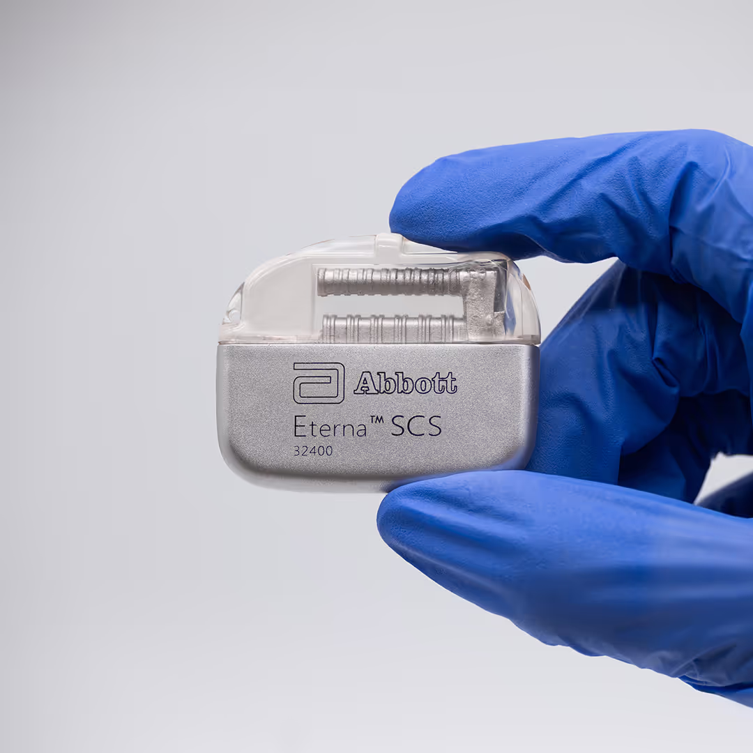 Dispositivo médico Eterna™ SCS da Abbott sendo segurado por uma mão com luva azul. O aparelho é um gerador de pulso implantável usado na terapia de estimulação da medula espinhal para dor crônica.
